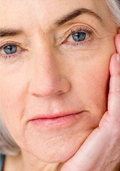 Up close shot of mature woman's face while she is looking directly at the camera and holding her cheek in her palm.