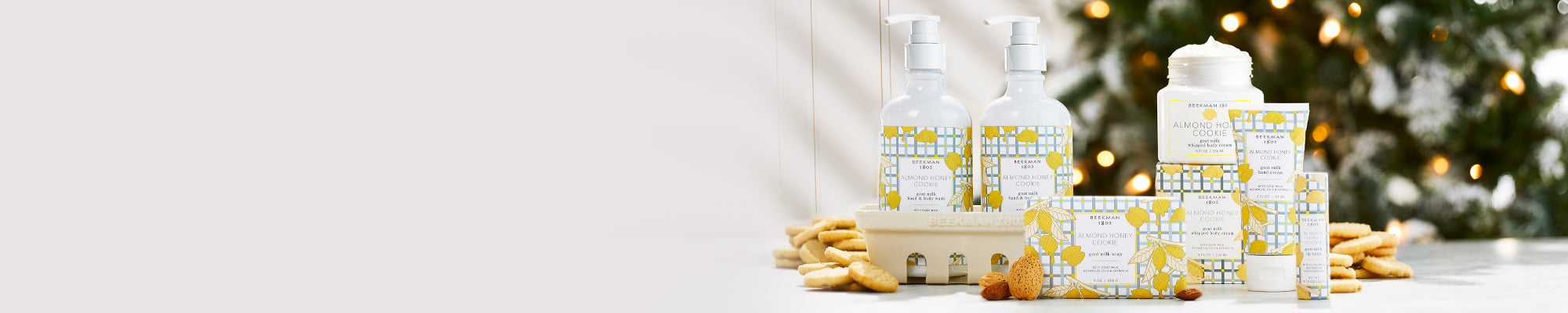 Collection shot of Beekman 1802's Almond honey Cookie bodycare products surrounded by cookies and a christmas tree in the background on the far right of the image.