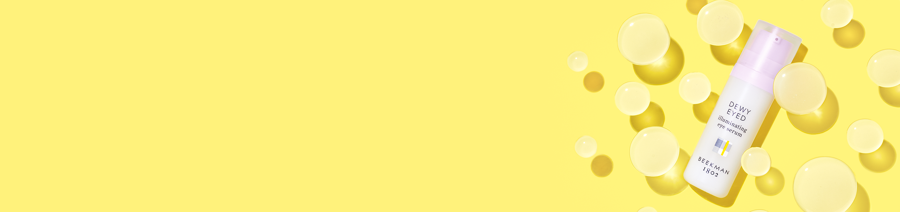 Bottle of Beekman 1802's Dewy Eyed Illuminating Eye Serum to the far right of the screen, surrounded by round clear gel orbs on a yellow background.