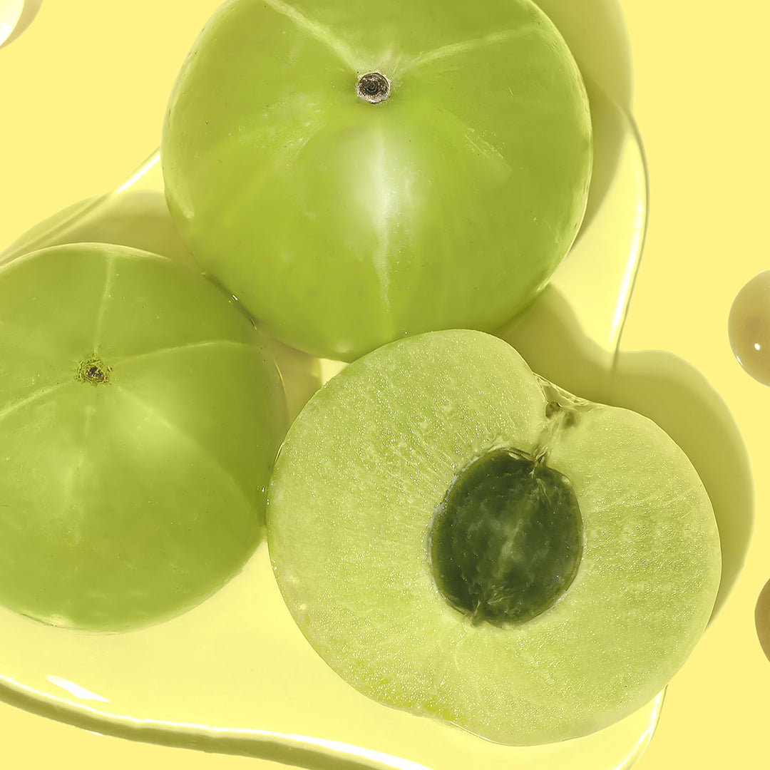 Up close shot of 2 full Amla Berries and one sliced in half to show the cross-section on a yellow background. 