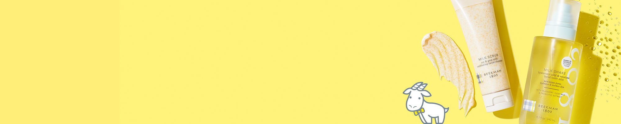 Bottle of Beekman 1802's Milk Shake and Tube of Beekman 1802's Milk Scrub on the far right hand side of the image, next to their texture swatch on a yellow background, with Goatie in a yellow bowtie in the foreground. 